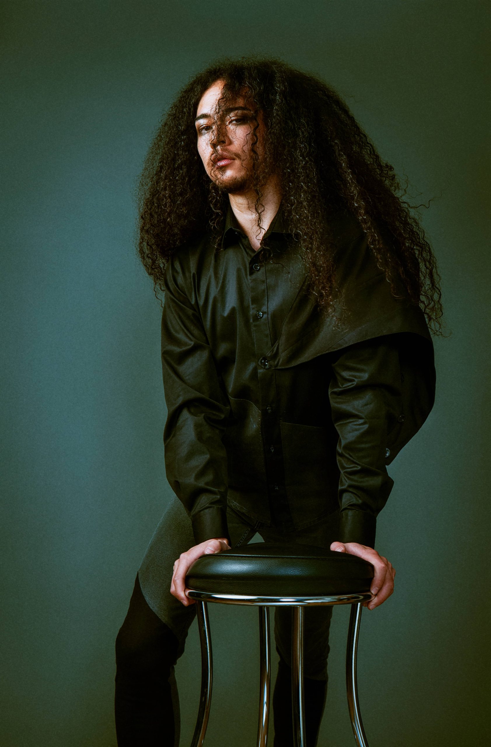 Man leaning on stool in black shirt and jeans