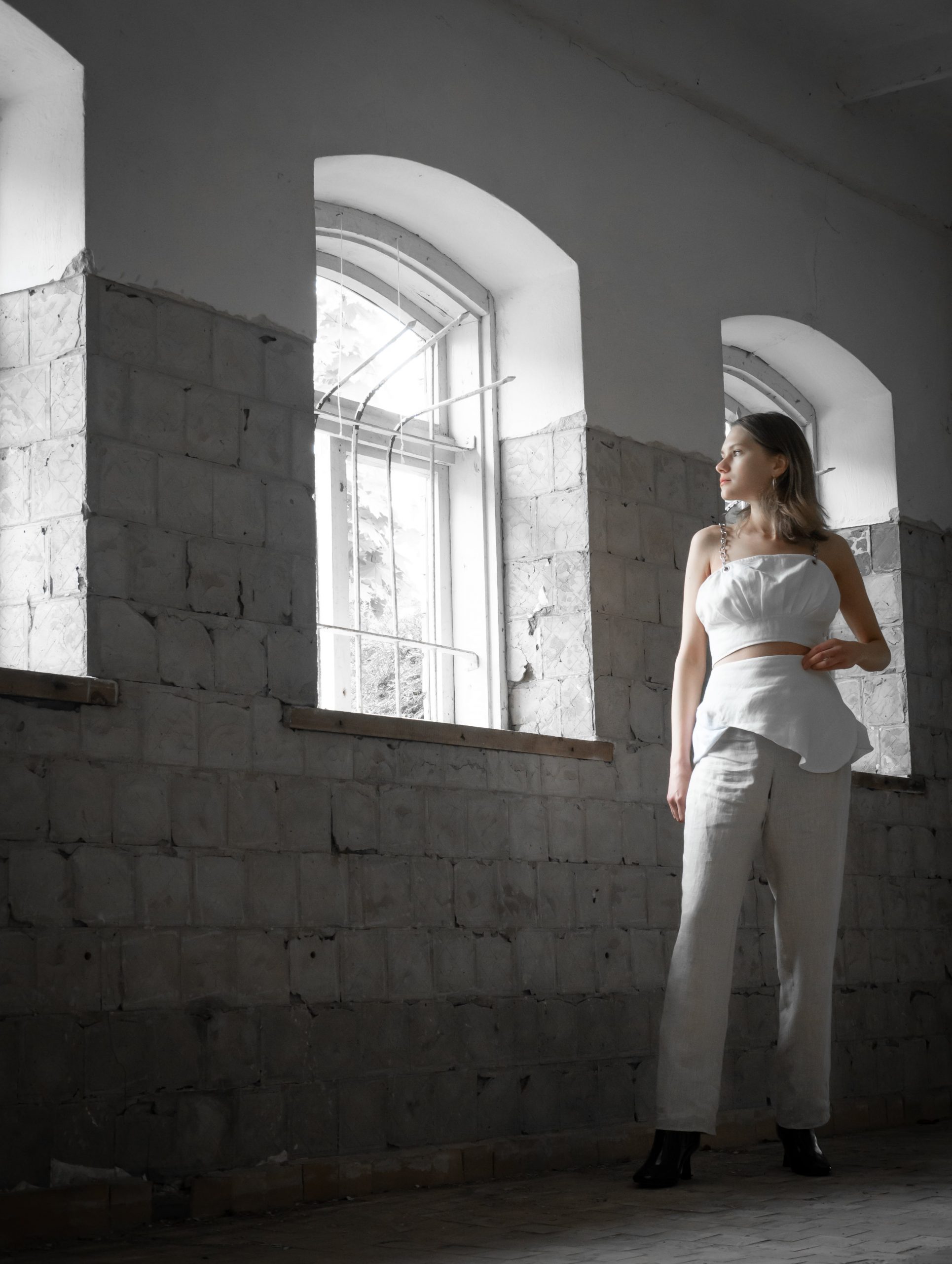 Blond girl in white top, white skirt and white pants - standing next to a concrete wall.