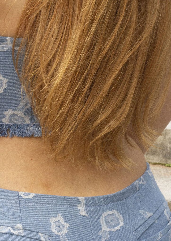 Detaljbilde av baksiden på en bukse og kort topp i blått materiale med hvite blomsterdetaljer.